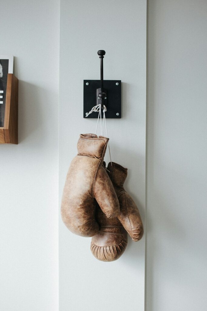 Vintage brown leather boxing gloves hang from a wall hook.